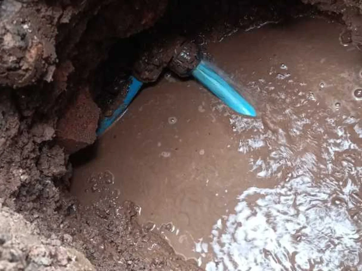 A leaking 25 mm blue MDPE supply pipe and its elbow fitting, exposed in a flooded excavation with water still escaping
